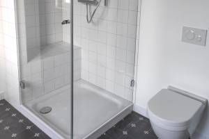 Badezimmer mit heller Dusche und Toilette und dunklem Fliesenboden
